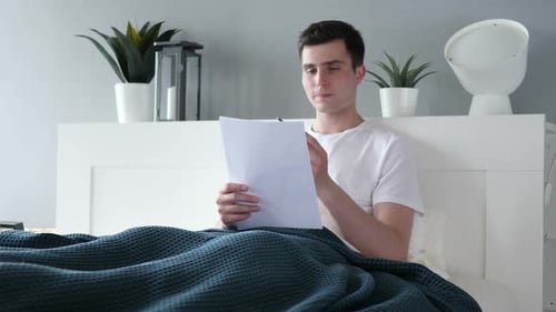 Man Studying Document in Bed With Pen