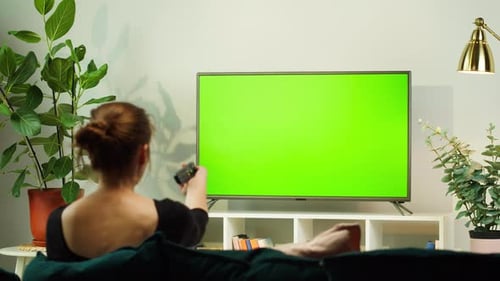 Woman Watching TV with Green Screen in Living Room Back View