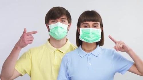 Young Couple Wearing Surgical Masks Pointing at Masks