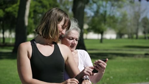 Grandmother and Granddaughter Using Phone in Park