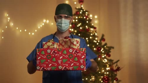 Medical Worker Holding Christmas Gifts in Front of Tree