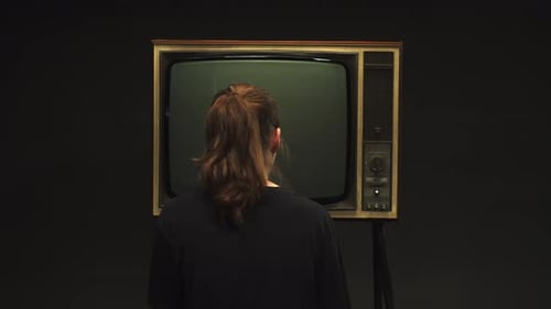 Young Woman Turning on Old Retro Television on Black Background Searching for a Signal Channel