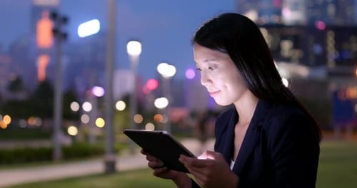 Woman Works on Tablet at Night in Urban Park