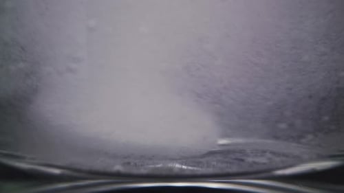 Round Vitamin Pill in Water with Numerous Spinning Bubbles