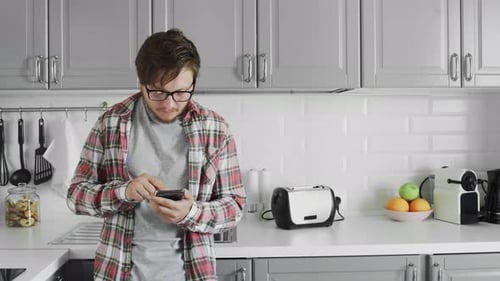 Young Man Using Smartphone in Modern Bright Kitchen