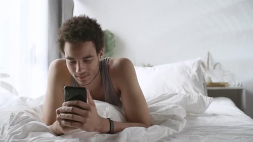 Man Lying in Bed Looking at Smartphone