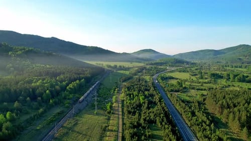 Trilhos de trem e uma rodovia no meio da floresta e das montanhas.