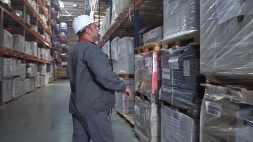 Im Logistiklager schaut der Arbeiter auf die Kisten und schreibt Notizen