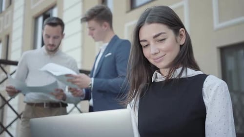 Porträt einer hübschen jungen Frau im Vordergrund, die mit Laptop arbeitet. Zwei erfolgreiche selbstbewusste Männer