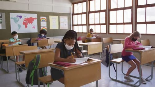 Group of kids wearing face masks writing while sitting on their desk at school
