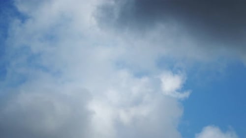 The movement of white clouds against the blue sky.