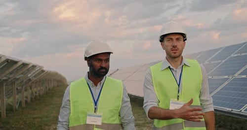 Diverse Ethnicity Male Engineers Communicating While Walking at Solar Panels Farm. Men in Uniform