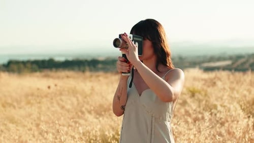Woman Filming with Vintage Camera in Golden Field