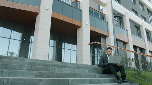 Portrait of Middleaged Entrepreneur Typing with Laptop Sitting on Office Center Stairs