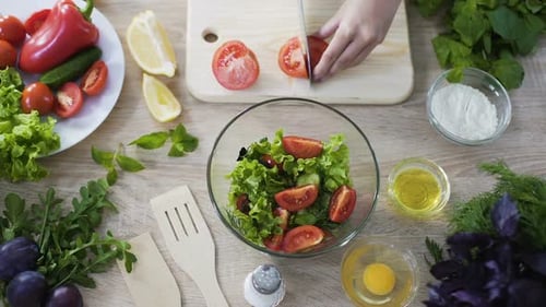 Draufsicht einer Köchin, die Tomaten schneidet und mit frischem Salat in eine Schüssel gibt
