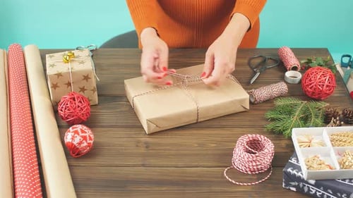 Woman Tying Twine Around Christmas Present on Table