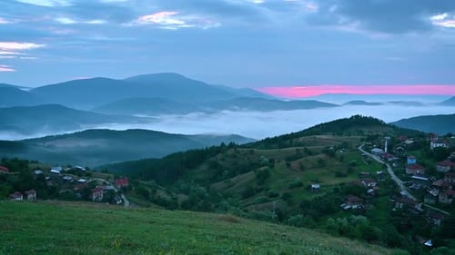 Blick auf den Sonnenaufgang und Morgennebel über den Berghängen und einem kleinen Dorf