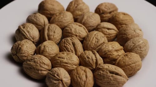 Cinematic, rotating shot of walnuts in their shells on a white surface