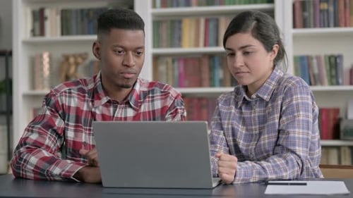 Young Adults Collaborating on Laptop Near Bookshelf