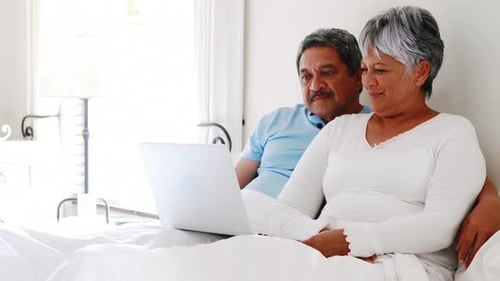 Happy Couple Relaxing in Bed with a Laptop