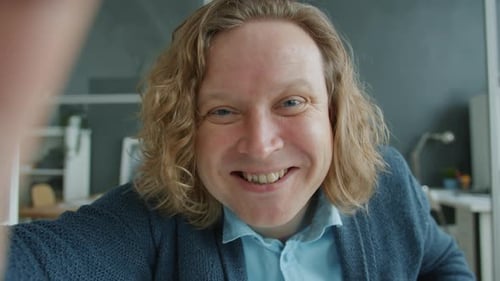Portrait of Cheerful Young Man Talking Online Looking at Camera Gesturing in Office