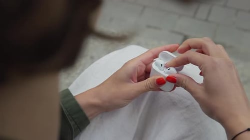 Woman Inserts Wireless Earbud in Ear Outdoors
