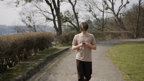 Teen Using Phone While Walking in Park