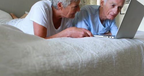 Senior Couple Use Laptop Together on Bed