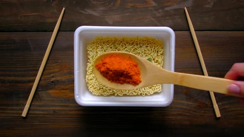 Adding Spice to Bowl of Noodles on Table
