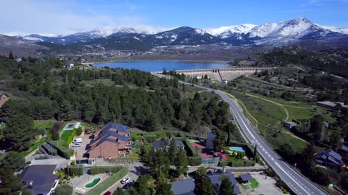 Smooth cinematic push in aerial over the town of Navacerrada towards the reservoir and the snow-capp