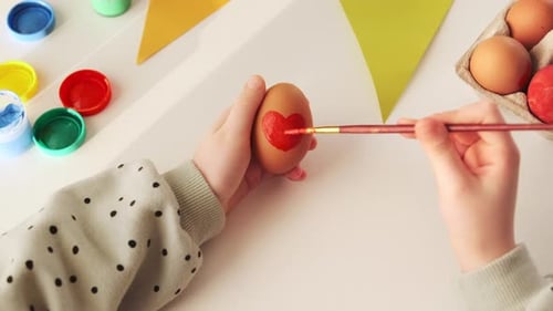 Little child decorates Easter eggs with colored food paint. Hand craft preparing for the feast