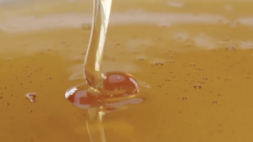 Macro close up shot of honey getting poured into honey on a plane surface. Abstract shot with endles