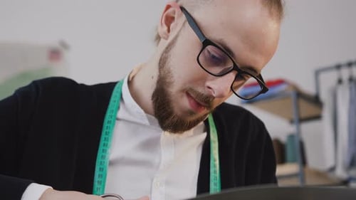 Jeune designer barbu ou tailleur de lunettes assis sur un lieu de travail