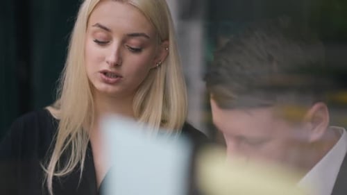 Portrait en gros plan d'une femme concentrée parlant avec un homme écrivant des notes sur une porte vitrée dans un bureau