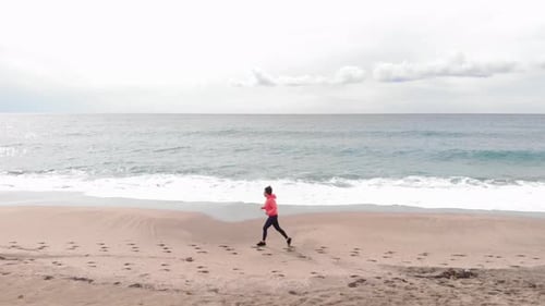 Female is running on empty beach at seaside surf, waves are splashing and foaming