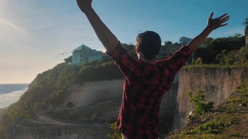 Young Man Traveler Raising His Hands High on Top of the Mountain Above Beautiful Landscape on Golden