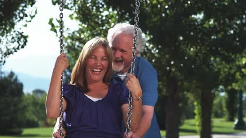 Older man pushing his wife on a swing.
