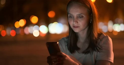 At Night, a Young Girl Holds a Smartphone in Her Hands and Looks at the Screen