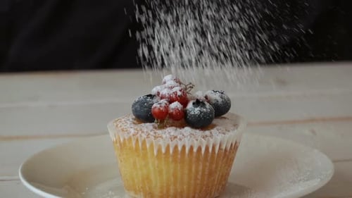 Powdered Sugar Falling Onto Berry-Topped Muffin