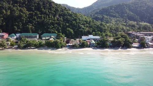 The green hills of the island are covered with palm trees, the sky is cloudy