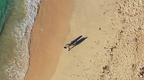 Romantic couple walking along the sandy beach leaving footprints, foamy waves washing the shore, hig