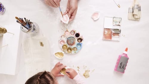 Mother and Daughter Painting Seashells at Table