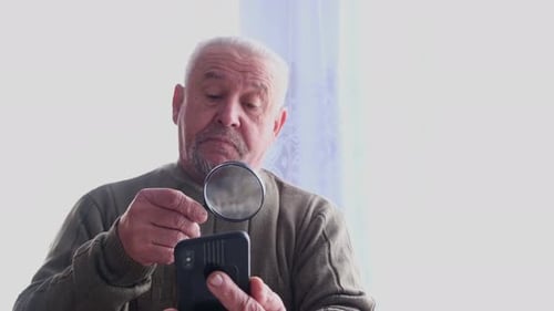 Senior Man Examining Phone with Magnifying Glass