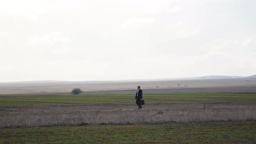 Geschäftsmann in Anzug und Tasche, der auf dem Feld spaziert.