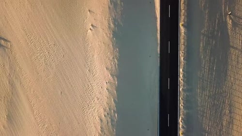 Above view of black asphalt road with desert and sand dunes around - travel roadtrip concept