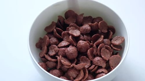 Chocolate Cereal Being Poured into a White Bowl