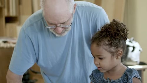 Older gentleman helping young girl and boy in a wood shop.