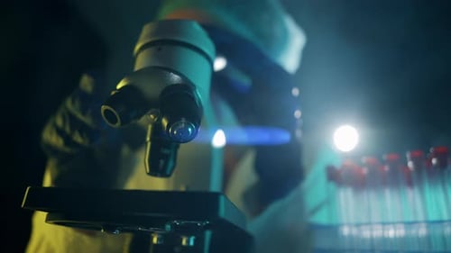 Scientist Adjusting Microscope in Dark Lab at Night