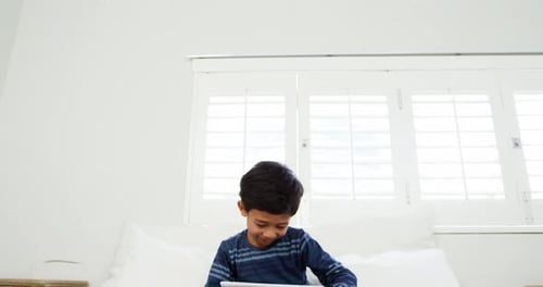 Boy using digital tablet while relaxing on bed