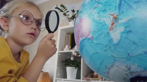 Girl Studies Globe With Magnifying Glass Indoors
